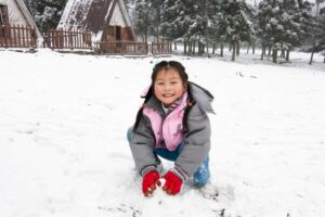 young girl posing for the camera while patting down snow
